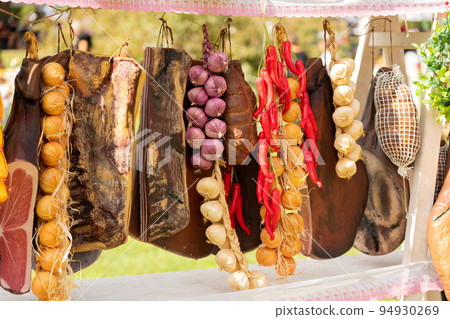 Smoked country meat, bacon, jamon and other delicacies hanging on the shop counter Smoked country meat, bacon, jamon and other delicacies hanging on the shop counter 94930269