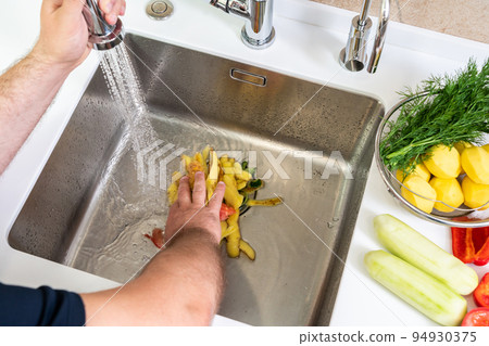 A hand shoves food waste into a disposer hole in the kitchen sink A hand shoves food waste into a disposer hole in the kitchen sink 94930375