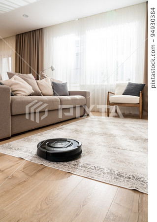 Vertical shot of a black robotic vacuum cleaner in a new living room in light beige and gray tones 94930384