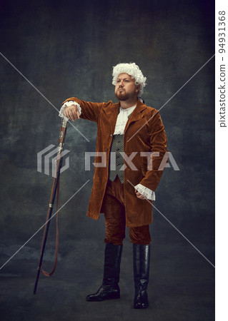 Creative portrait of retro style hunter in vintage hunting clothing with old gun isolated over dark background. Art, fashion, emotions, traditions, hobby concept 94931368