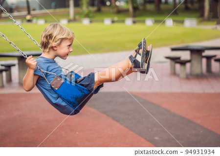 Funny kid boy having fun with chain swing on outdoor playground. child swinging on warm day. Active leisure with kids. Boy wearing casual colorful school kid clothes Funny kid boy having fun with chain swing on outdoor playground. child swinging on warm day. Active leisure with kids. Boy wearing casual colorful school kid clothes 94931934