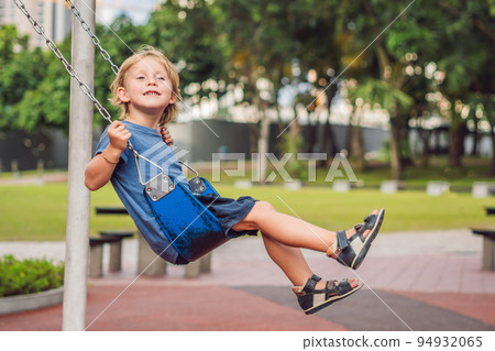 Funny kid boy having fun with chain swing on outdoor playground. child swinging on warm day. Active leisure with kids. Boy wearing casual colorful school kid clothes 94932065