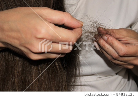 A girl with long dark hair holds a bunch of fallen hair in her hands. Hair loss problem. 94932123
