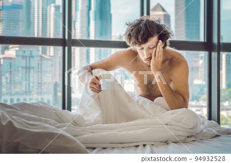 Man wakes up in the morning in an apartment in the downtown area with a view of the skyscrapers and drinks coffee. Life in the noise of the big city concept. Not enough sleep 94932528