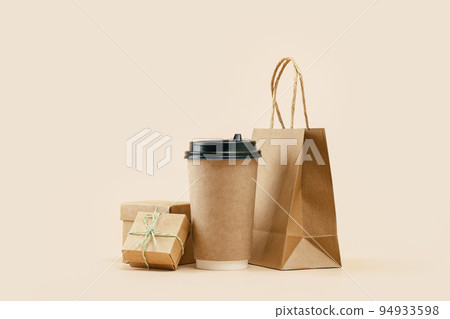 Takeaway paper coffee cup with lunch bag and bonus gift box on beige. Snack delivery service. Coffee to go. Grab and go or carry out beverage. Disposable mockup packaging. Place for text. Minimal 94933598