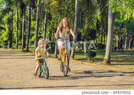 Happy family is riding bikes outdoors and smiling. Mom on a bike and son on a balancebike 94934002