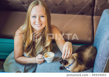 Young woman is drinking coffee and stroking the cat 94934003