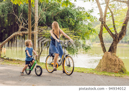 Happy family is riding bikes outdoors and smiling. Mom on a bike and son on a balancebike 94934012