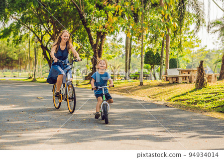 Happy family is riding bikes outdoors and smiling. Mom on a bike and son on a balancebike 94934014