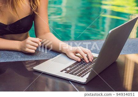 Young female freelancer sitting near the pool with her laptop in the hotel browsing in her smartphone. Busy at holidays. Distant work concept. Copy space for your text 94934051