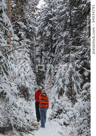 Couple in winter clothing, man and woman in red sweaters walking through the snow covered trees, winter wonderland Couple in winter clothing, man and woman in red sweaters walking through the snow covered trees, winter wonderland 94934791