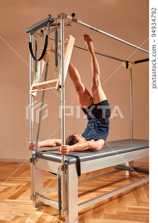 Fit man doing a lunge stretch yoga pilates exercise to strengthen and tone his muscles using a reformer in gym. Health and fitness concept Fit man doing a lunge stretch yoga pilates exercise to strengthen and tone his muscles using a reformer in gym. Health and fitness concept 94934792