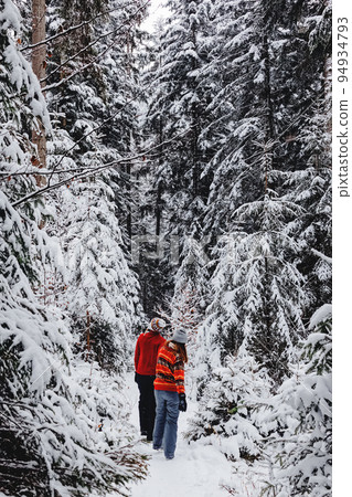 Couple in winter clothing, man and woman in red sweaters walking through the snow covered trees, winter wonderland, Christmas holidays Couple in winter clothing, man and woman in red sweaters walking through the snow covered trees, winter wonderland, Christmas holidays 94934793