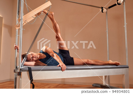 Fit man doing a lunge stretch yoga pilates exercise to strengthen and tone his muscles using a reformer in gym. Health and fitness concept 94934801