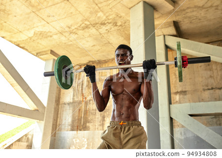 Athletic black young man lifting a heavy-weight barbell in outdoor gym under the bridge. Healthy lifestyle concept 94934808