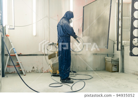 worker powder coats steel parts in a spray booth 94935052
