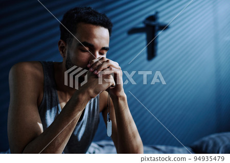 Young depressed man with metallic medallions on chain in his hands praying 94935479