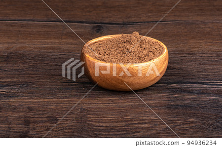 Wooden bowl full of ground cinnamon on a wooden background with space for text. 94936234