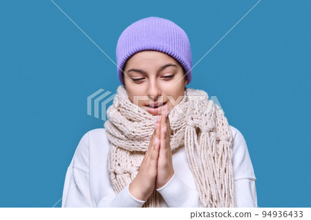 Winter portrait of young female in sweater hat scarf, on blue studio background 94936433