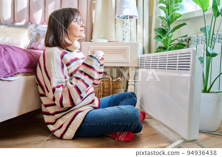 Woman warming herself in bedroom near electric heater Woman warming herself in bedroom near electric heater 94936438