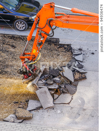An excavator breaks up the old asphalt layer with a bucket during street repairs An excavator breaks up the old asphalt layer with a bucket during street repairs 94936474