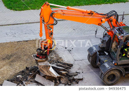 An excavator breaks up the old asphalt layer with a bucket during street repairs An excavator breaks up the old asphalt layer with a bucket during street repairs 94936475