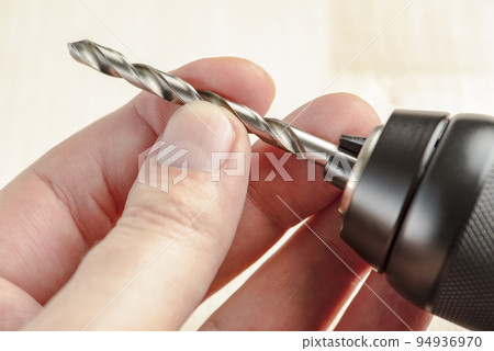 Installing a drill bit in a drill, hands take a drill and install it in a cordless drill chuck Installing a drill bit in a drill, hands take a drill and install it in a cordless drill chuck 94936970