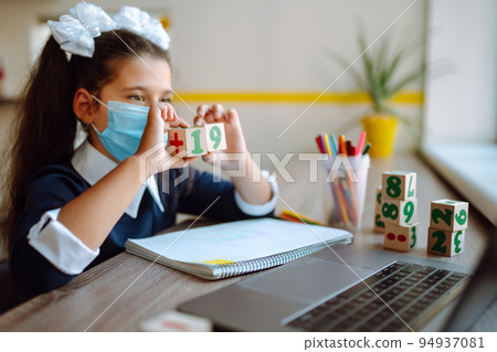 School girl in medical mask using laptop computer studying through online e-learning system. 94937081