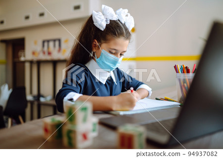 School girl in medical mask using laptop computer studying through online e-learning system. 94937082