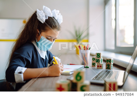 School girl in medical mask using laptop computer studying through online e-learning system. School girl in medical mask using laptop computer studying through online e-learning system. 94937084