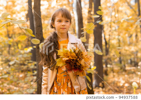 Little kid girl with autumn orange leaves in a park. Lifestyle, fall season and children concept. Little kid girl with autumn orange leaves in a park. Lifestyle, fall season and children concept. 94937588