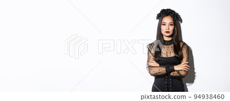 Image of beautiful asian woman in black lace dress and wreath looking serious. Girl dressed-up for halloween party as evil witch, standing over white background Image of beautiful asian woman in black lace dress and wreath looking serious. Girl dressed-up for halloween party as evil witch, standing over white background 94938460