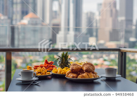 Breakfast table with coffee fruit and bread croisant on a balcony against the backdrop of the big city 94938468