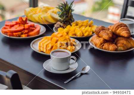 Breakfast table with coffee fruit and bread croisant on a balcony against the backdrop of the big city Breakfast table with coffee fruit and bread croisant on a balcony against the backdrop of the big city 94938471
