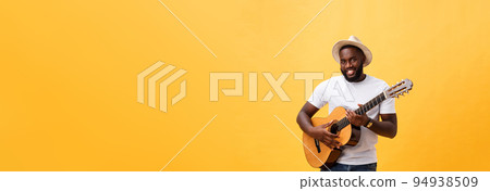 Muscular black man playing guitar, wearing jeans and white tank-top. Isolate over yellow background. 94938509