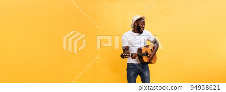 Full-length photo of excited artistic man playing his guitar. Isolated on yellow background. Full-length photo of excited artistic man playing his guitar. Isolated on yellow background. 94938621