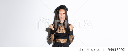 Image of joyful attractive asian witch, female in halloween costume yelling in rejoice and fist pump, celebrating victory, triumphing over white background Image of joyful attractive asian witch, female in halloween costume yelling in rejoice and fist pump, celebrating victory, triumphing over white background 94938692