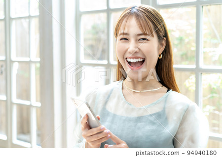 一個年輕女子在明亮的窗戶旁使用智能手機 94940180