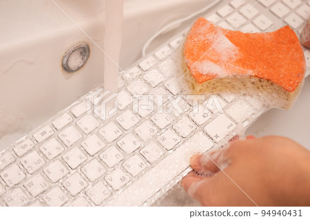 Woman washing white computer keyboard with a sponge with foam. Woman washing white computer keyboard with a sponge with foam. 94940431