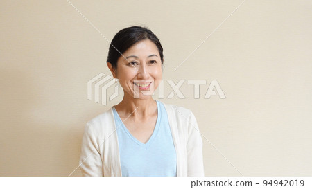 一位微笑的中年婦女，身穿淺藍色 T 恤和白色開衫 94942019