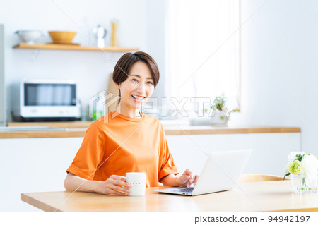 A middle-aged housewife looking at a computer in the kitchen dining room A middle-aged housewife looking at a computer in the kitchen dining room 94942197
