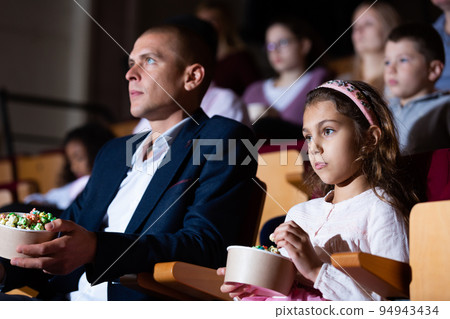 Tween girl with father watching movie in cinema Tween girl with father watching movie in cinema 94943434