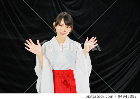A Japanese woman in shrine maiden clothes spreads her hands 94943882