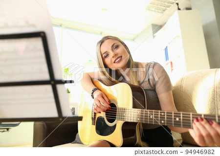 Smiling blond woman playing guitar and looking through notes Smiling blond woman playing guitar and looking through notes 94946982
