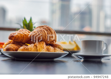 Breakfast table with coffee fruit and bread croisant on a balcony against the backdrop of the big city 94947248