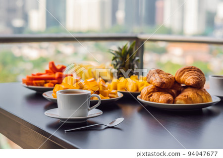 Breakfast table with coffee fruit and bread croisant on a balcony against the backdrop of the big city 94947677