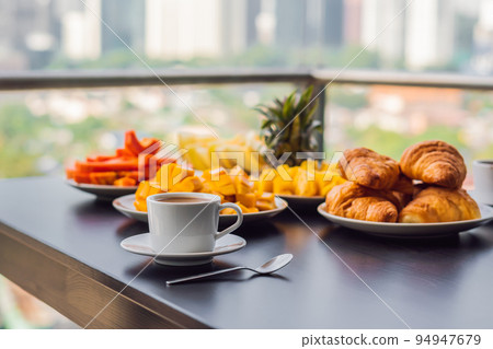 Breakfast table with coffee fruit and bread croisant on a balcony against the backdrop of the big city 94947679