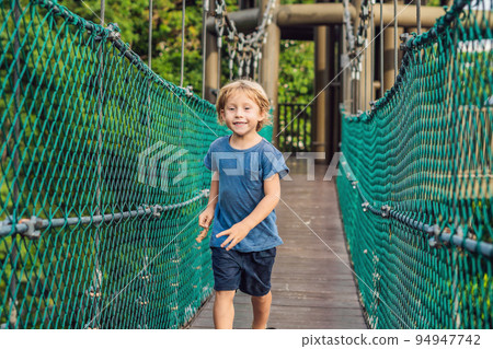 The boy is running on a suspension bridge in Kuala Lumpur, Malaysia The boy is running on a suspension bridge in Kuala Lumpur, Malaysia 94947742