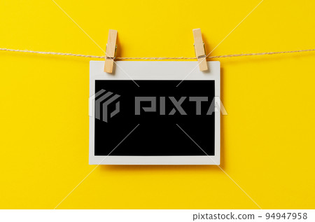 An empty photo is hanging on a rope with a clothespin. A design element. Yellow background. Copy space. 94947958