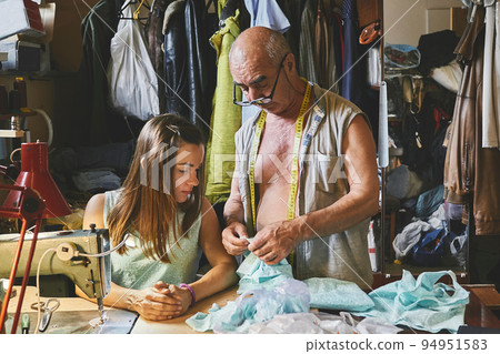 Senior experienced master tailor teaches a young girl seamstress how to sew Senior experienced master tailor teaches a young girl seamstress how to sew 94951583